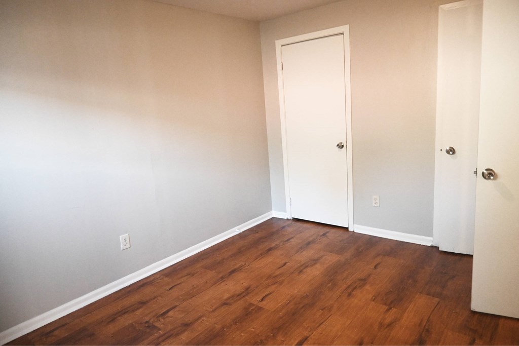 A room with a white door and wood flooring.