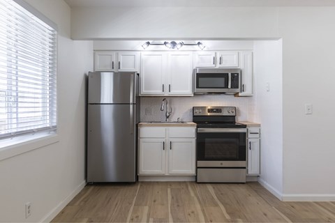 A kitchen with a stainless steel refrigerator, microwave, oven, and wooden floors.