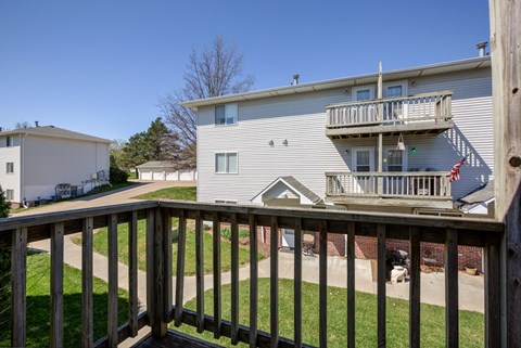 A wooden deck overlooks a grassy area and a two-story building.