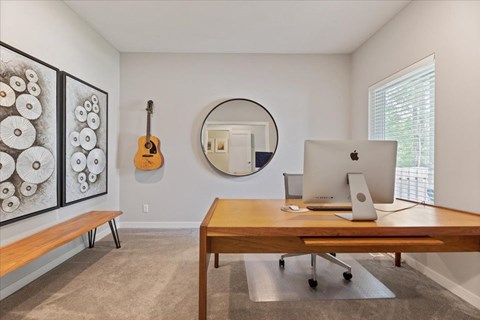 A room with a wooden desk and a guitar hanging on the wall.
