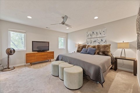 A bedroom with a bed, a dresser, a television, and a ceiling fan.