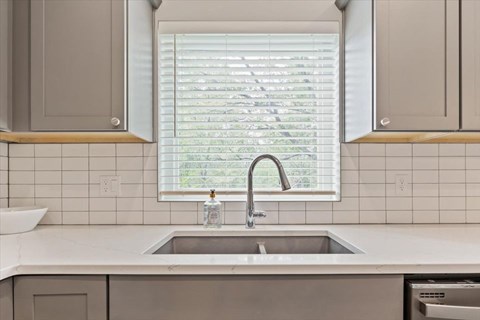 A kitchen with a sink and a window with blinds.