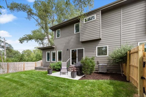 A grey house with a wooden fence and a green lawn.