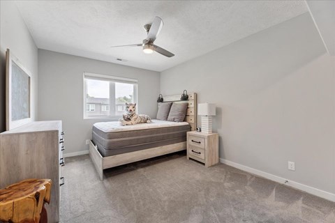 A bedroom with a bed, nightstand, and a window with a dog on the windowsill.
