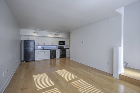 A kitchen with white walls and wooden floors with sunlight shining through the window.