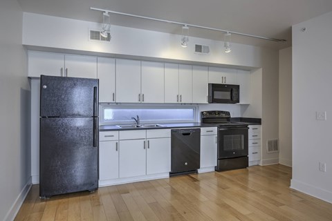 A kitchen with a black fridge, white cabinets, and wooden floors.