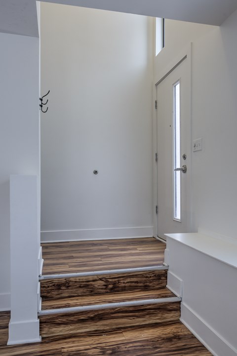 A white door is on the right side of a room with wooden stairs.