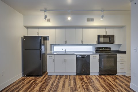 A kitchen with a black refrigerator, white cabinets, and a wooden floor.