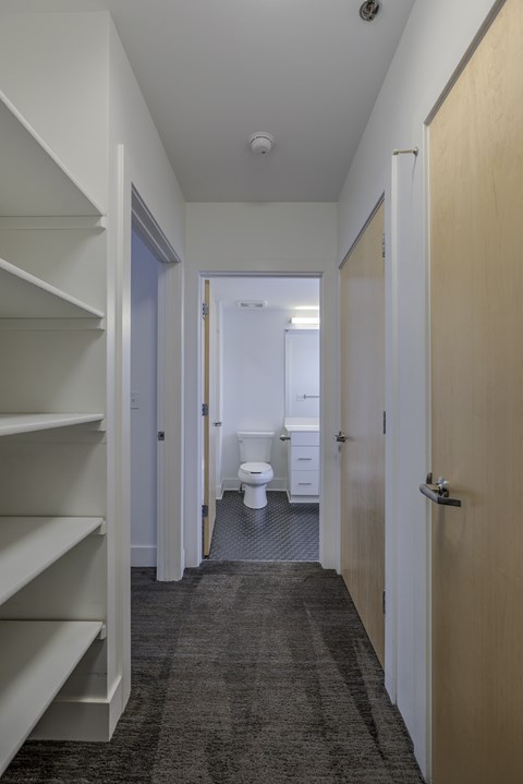 A hallway with a toilet and sink in the background.