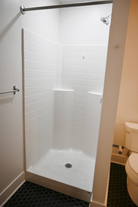 A white tiled shower stall with a drain in the middle.