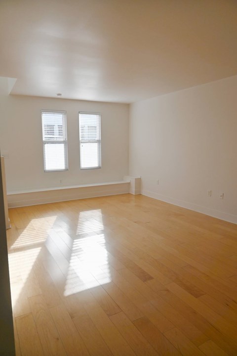 A room with wooden floors and two windows letting in sunlight.