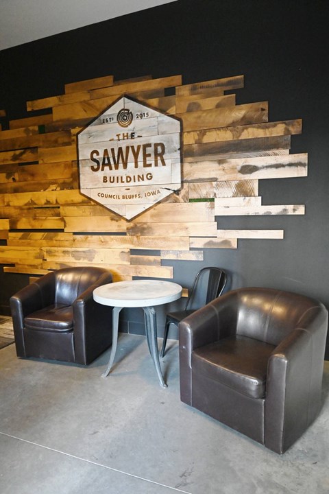 Two black leather chairs are placed in front of a wooden sign that says "The Sawyer Building".