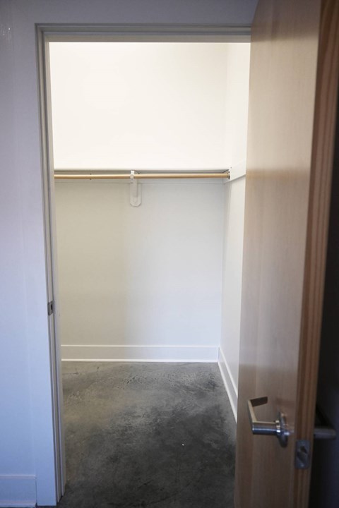 A white door with a silver handle is open to a room with a white wall and a brown door.