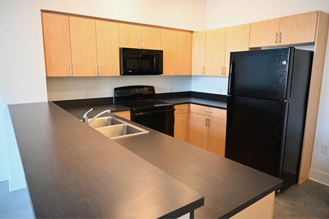 A black refrigerator sits in a kitchen with wooden cabinets and a black oven.
