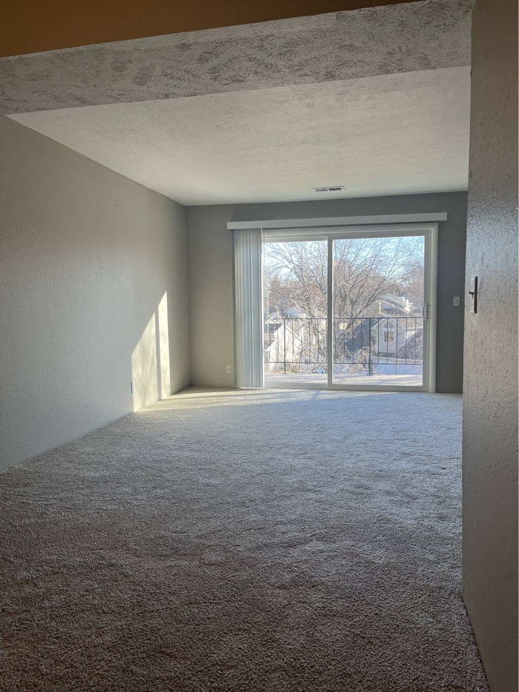 A room with a carpeted floor and a sliding glass door leading outside.