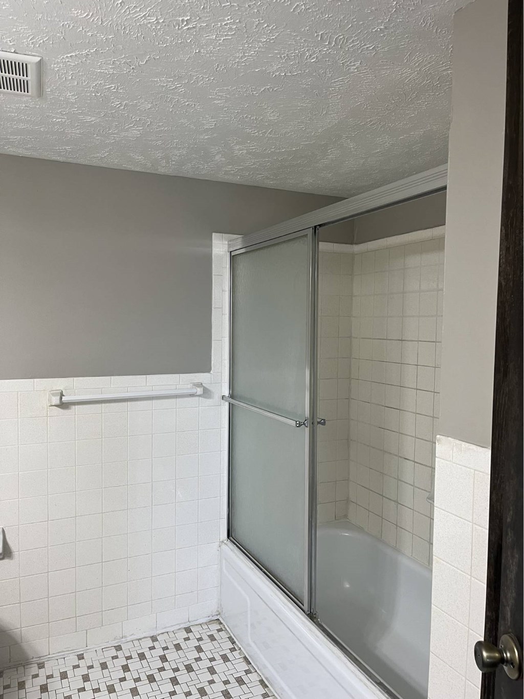 A white tiled bathroom with a glass shower door.