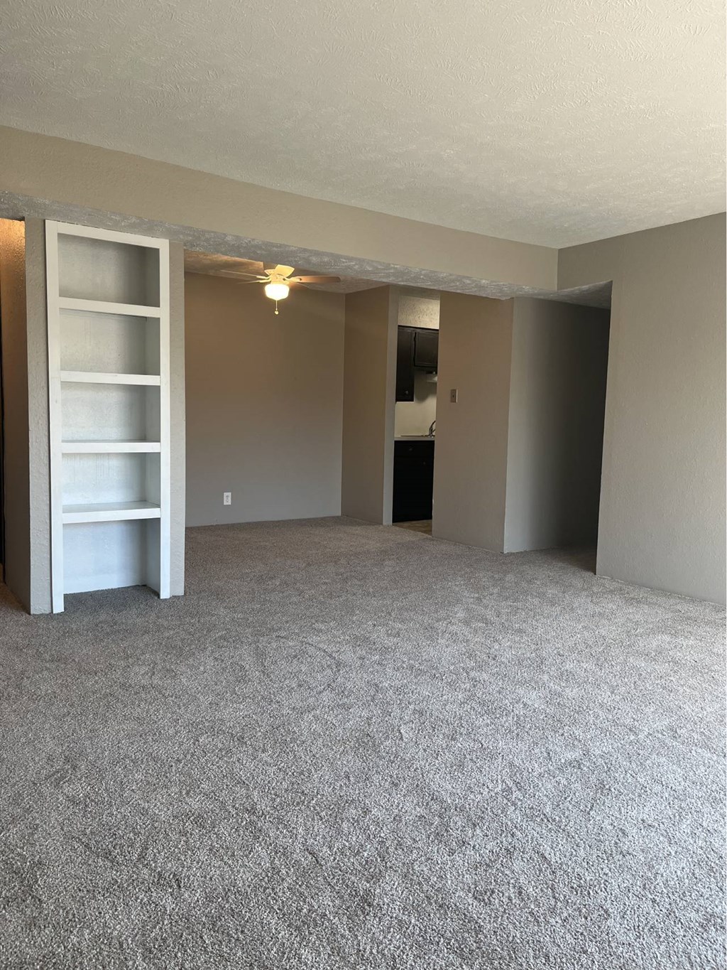 A room with a grey carpet and a white shelf unit.