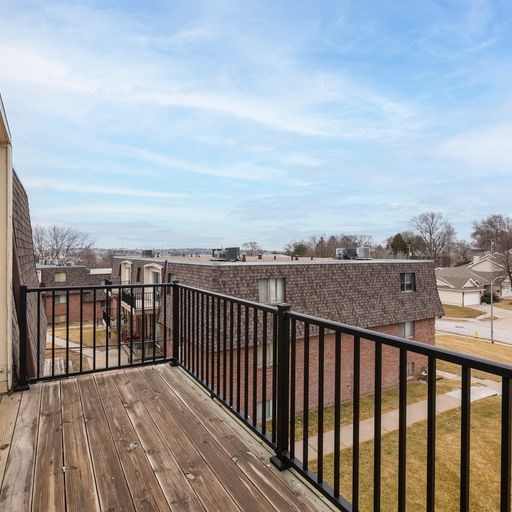 A balcony with a black railing overlooks a residential area.