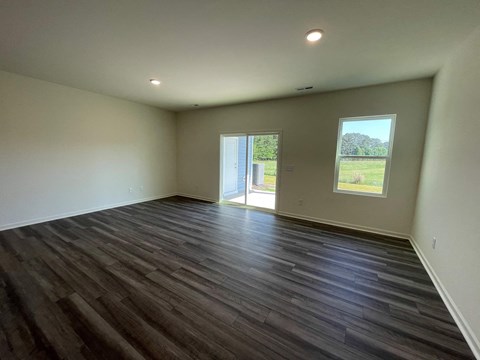 A room with wooden flooring and a view of a grassy field through a window.