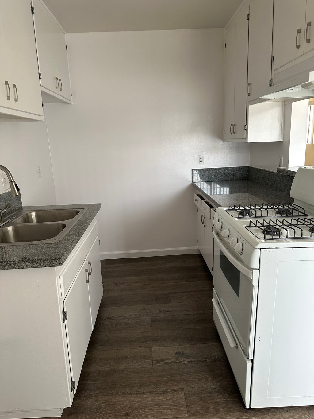A white kitchen with a stove, sink, and cabinets.