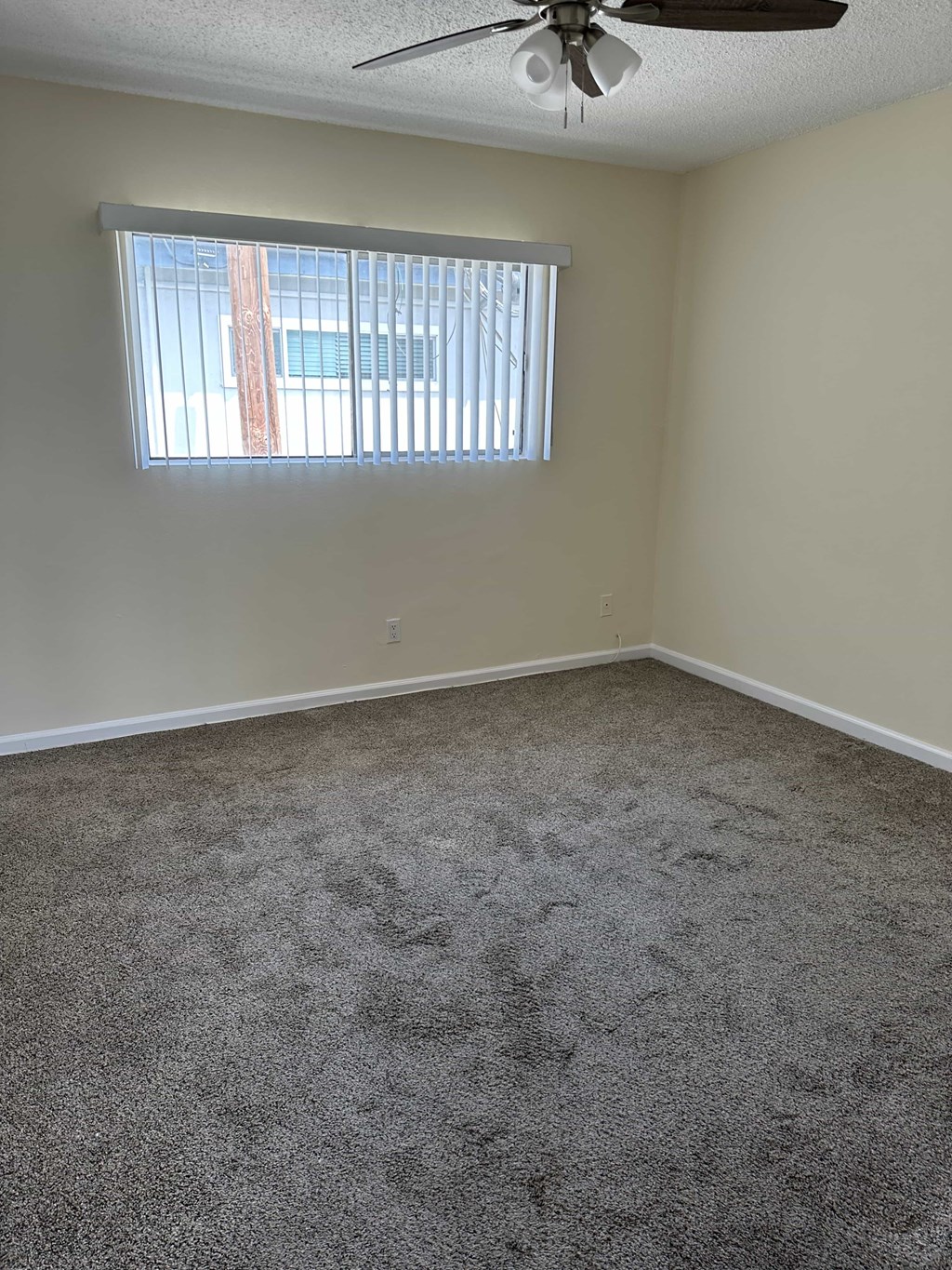 A room with a ceiling fan and a window with blinds.