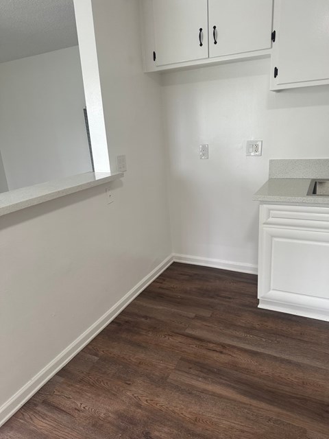 A kitchen with white cabinets and a wooden floor.