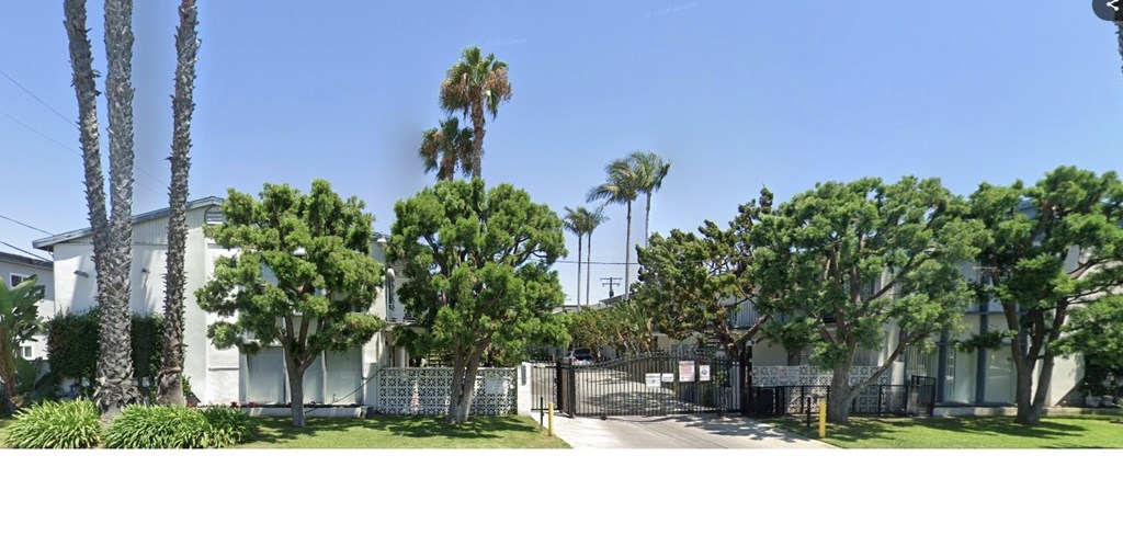 A white building with a gate and trees in front.