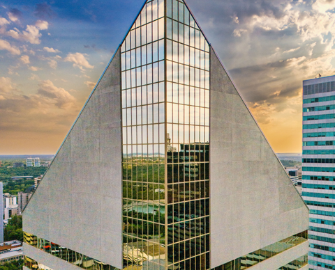 A modern building with a triangular glass facade is reflected in its own windows.