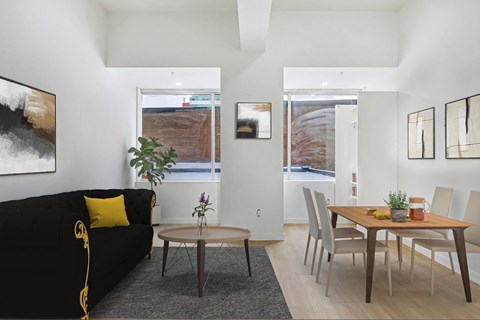 A black couch with yellow pillows sits in a living room with a dining table and chairs.