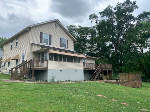 A house with a grey and beige exterior has a deck and a small tree in front.