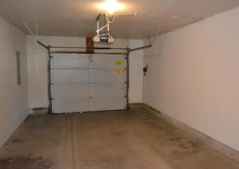 A white wall with a white door and a white ceiling with a light on it.