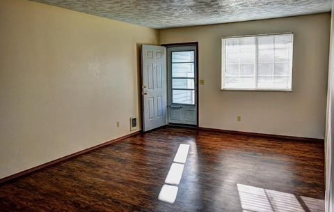 A room with a wooden floor and a door leading to another room.