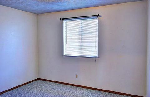 A room with a window covered by white blinds.