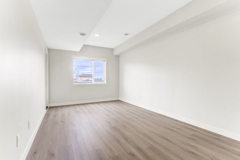 A room with wooden flooring and a window showing a view of a building.