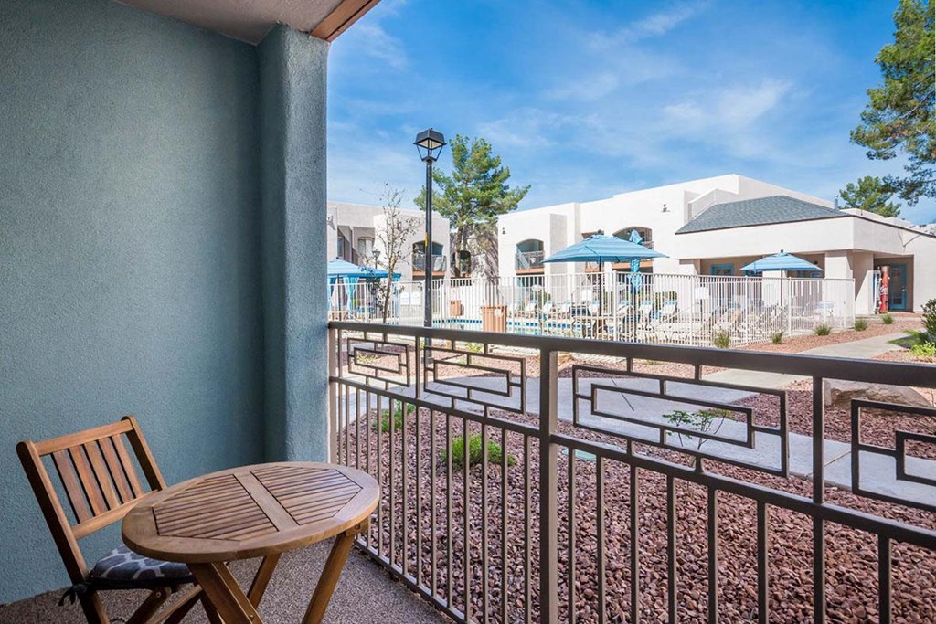 A balcony with a wooden chair and table overlooking a pool area.