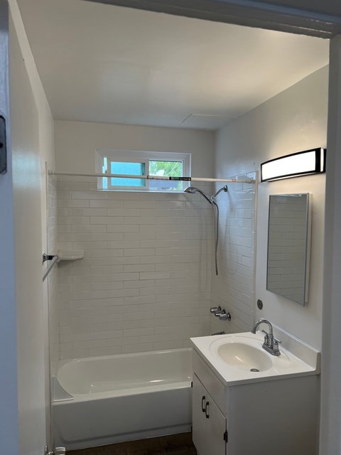 A white bathroom with a tub, sink, mirror, and a window.