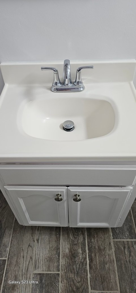 A white sink with a silver faucet and a white cabinet below it.