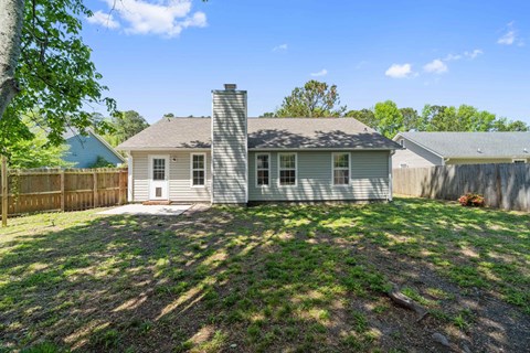 A house with a white door and a chimney is surrounded by a fence and trees.