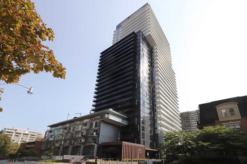 A tall building with a black and white striped facade stands in front of a tree with orange leaves.