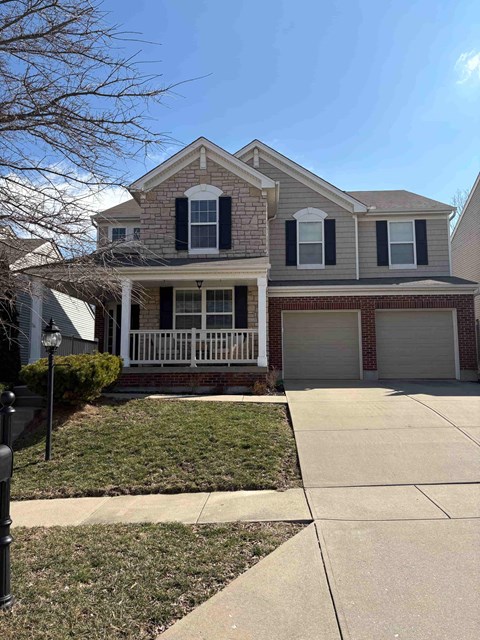 A two-story house with a white porch and a brick base.