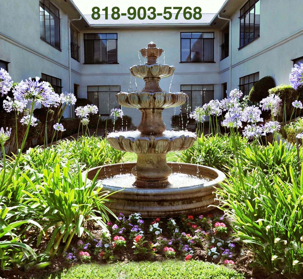 A fountain in the middle of a garden with a building in the background.