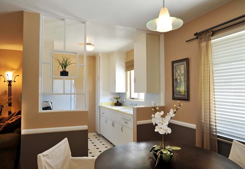 A dining room with a table set for two and a kitchen area in the background.