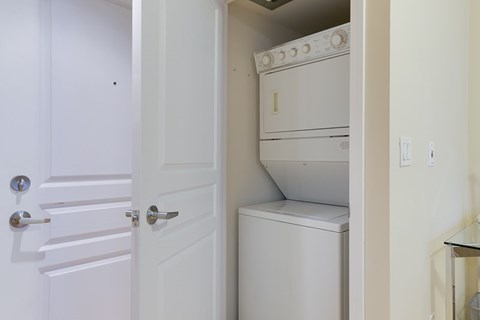 A white door is open to a small kitchen with a white oven and dishwasher.