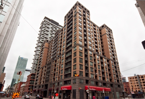 A large brown building with many windows is in the middle of a city street.