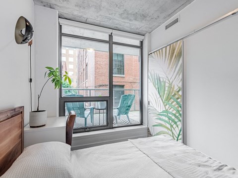 A bedroom with a large bed and a view of a balcony with chairs.