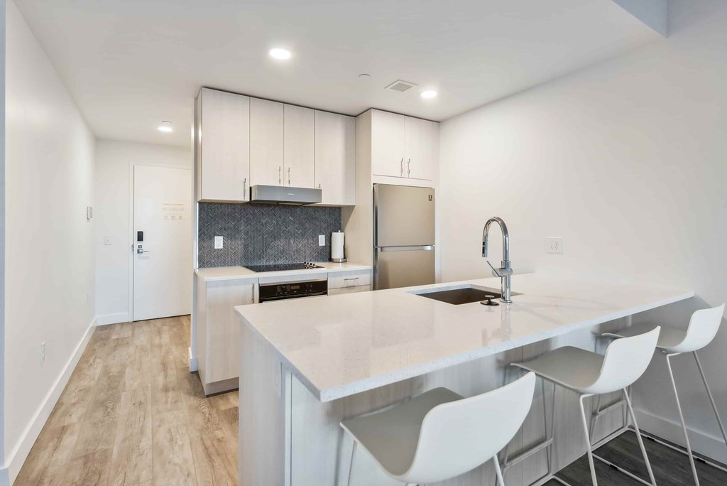 A kitchen with a white counter and white chairs.