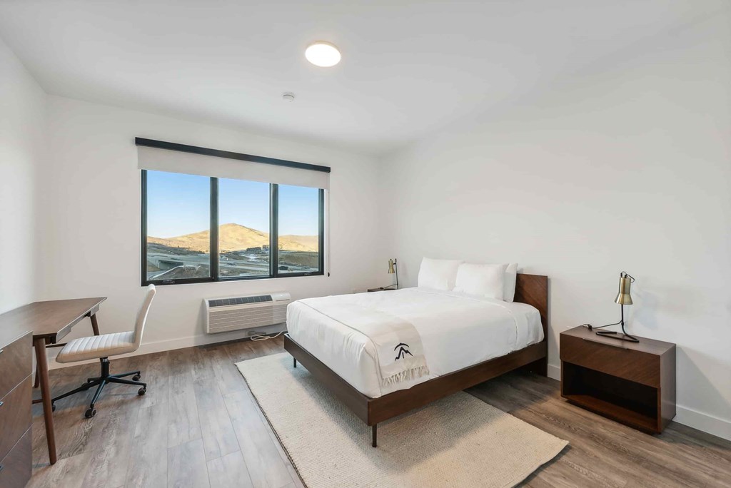 A bedroom with a large bed and a chair by a window overlooking a mountain.