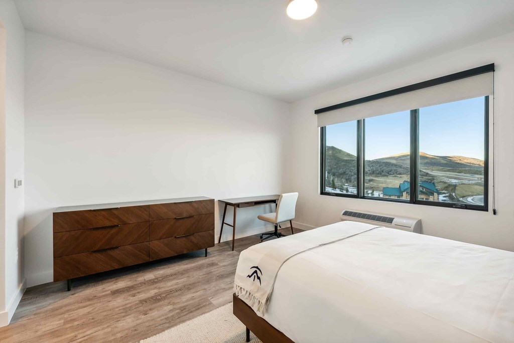 A bedroom with a large bed, a wooden dresser, and a window overlooking a landscape.