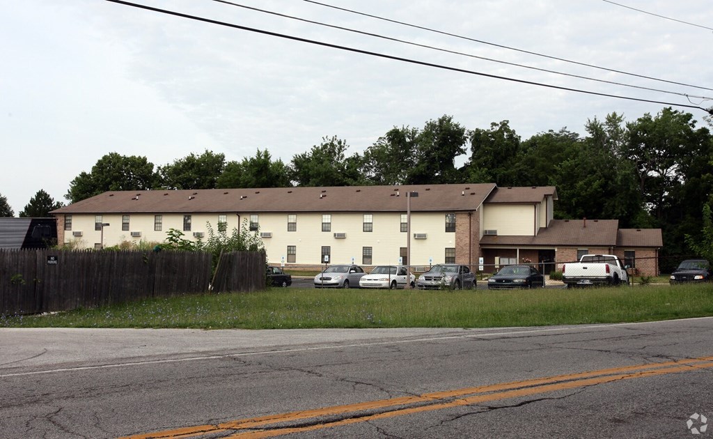 A large white building with a brown roof is surrounded by a wooden fence.