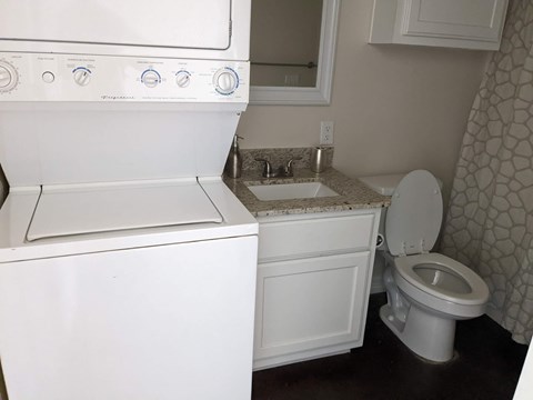 A white washing machine is in a laundry room with a toilet and sink.